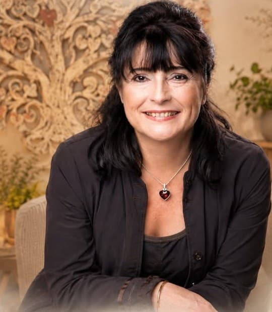Catherine Fournier, souriante, devant un arbre de vie sculpté